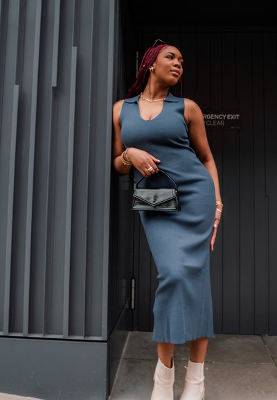 Vestido midi azul acanalado con cuello alto y silueta ajustada, combinado con un bolso negro texturizado y botines crema.