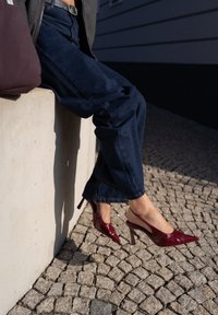 Sabrinas de couro verniz vermelho com bicos apontados e um salto alto fino, usadas com jeans de ganga de perna larga em azul escuro.