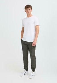 Valkoinen lyhythihainen t-paita, oliivinvihreät cargo-housut taskuilla ja valkoiset lenkkarit mustilla raidoilla. Yksinkertainen, rento asu.