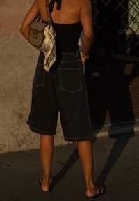Fekete denim szabott nadrág, laza fazonnal és feltekert szegéllyel. Fekete, testhezálló toppal és vállon átkötött mintás táskával viselve.