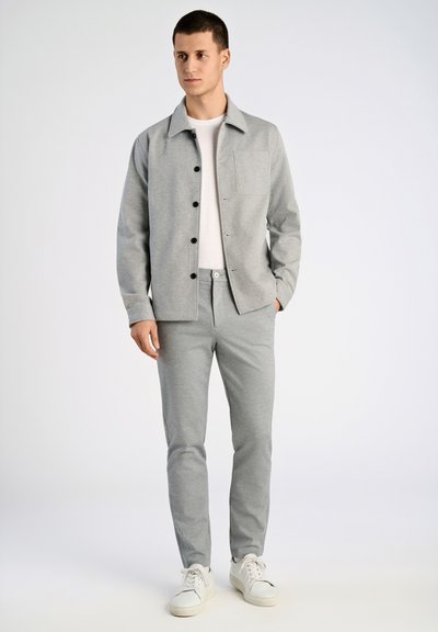 Chaqueta gris con cierre de botón y bolsillo frontal, combinada con pantalones grises. La tela parece suave y ambas prendas tienen un corte holgado.