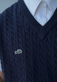 Ναυτικό πλεκτό γιλέκο με σχέδιο καλωδίου, που διαθέτει V-λαιμόκοψη και μικρό κεντητό λογότυπο κροκοδείλου στην αριστερή πλευρά.