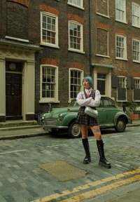 Πλατιά φούστα, λευκή μπλούζα με μακρύ μανίκι και μαύρες πλατφόρμες. Μια ασημένια τσάντα κόντρα με ένα vintage πράσινο αυτοκίνητο σε λιθόστρωτο δρόμο.
