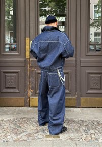 Denim jakna in ohlapne hlače temno modre barve, z izrazitimi šivi in verižnim detajlom na pasu. Tekstilirana tkanina.