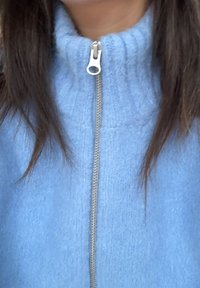 Pull bleu clair à fermeture éclair avec col montant, doté d'une fermeture éclair argentée et d'une texture côtelée. Tissu doux avec une apparence confortable.