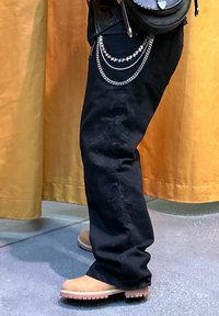 Pantalons noirs avec broderie florale, accents de chaînes métalliques et bottes beiges. Le tissu présente une texture lisse avec une coupe ample.