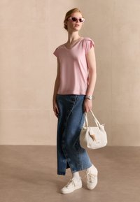 Lichtroze top met korte mouwen, denimrok met knopen, witte handtas, witte sneakers en roze zonnebril. Glad materiaal en casual pasvorm.