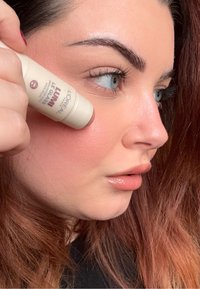 Iluminador en barra de L'Oréal con tubo beige, usado en la mejilla; textura suave, brillo ligero, realzando los rasgos faciales.