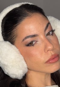 Zbliżenie na kobietę o brązowych oczach, noszącą białe puszyste nauszniki i błyszczącą różową szminkę, patrzącą lekko w bok.