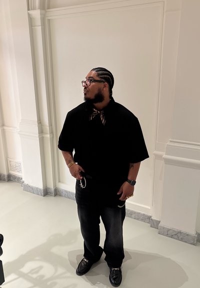 Camisa negra de manga corta, jeans oscuros y zapatos negros. Acento de una bufanda de patrón alrededor del cuello y una cadena de plata en el cinturón.