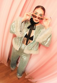 Ensemble étincelant en deux pièces argentées avec accents en fausse fourrure, comprenant une veste courte et un pantalon ajusté. Accessoires : lunettes de soleil uniques.