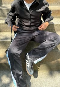 Svart långärmad tröja med Adidas-logga, tillsammans med svarta träningbyxor med ljusblå detaljer och vita sidoränder. Bärs med svarta sneakers.