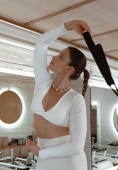 Top blanco de manga larga y ajustado con un escote pronunciado, combinado con pantalones blancos de cintura alta. Los accesorios incluyen un collar de cuentas colorido.