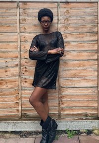 Juoda mini suknelė su blizgučiais, ilgomis rankovėmis, laisvo silueto ir permatoma tekstūra. Derinama su juodais odiniais batais iki kelių.