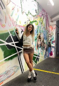 Vitt zip-up hoodie med grafik, brun minikjol och svarta plattformsskor. Styler med vita knästrumpor mot en färgglad muralbakgrund.
