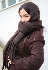 Rjavi volneni šal, ovit okoli vratu, z dolgimi, resastimi konci. Šal je usklajen z rjavim plaščem. Gladek tekstura.