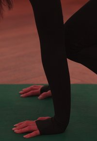 Persoană în colanți negri cu mâinile pe un covor de yoga verde, sprijinindu-se în poziția de plank sau flotare, la apus.