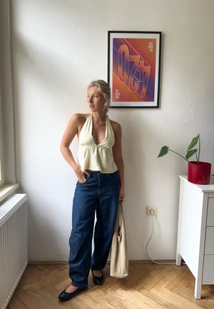 Top halter amarillo claro con detalle de plisado, combinado con jeans de pierna ancha en azul oscuro. Accesorios incluyen un bolso tote neutro y zapatos planos negros.
