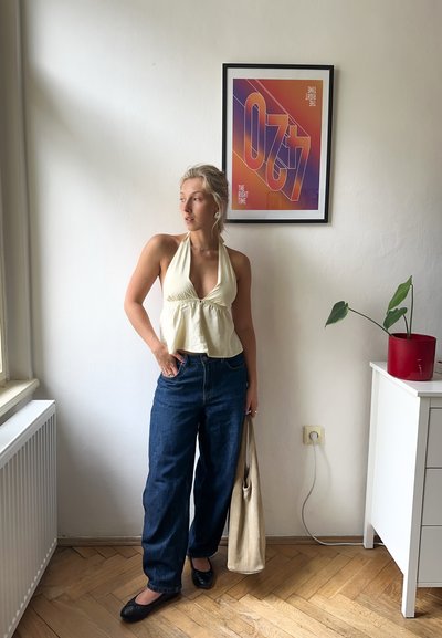 Top halter amarillo claro con detalle de plisado, combinado con jeans de pierna ancha en azul oscuro. Accesorios incluyen un bolso tote neutro y zapatos planos negros.