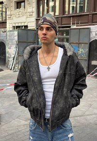 Črna jakna iz umetnega usnja z našivko z obrobo iz umetnega krzna na kapuci, z zadrgo in žepnimi manšetami. Nošena preko bele majice brez rokavov in spremenjenih kavbojk.