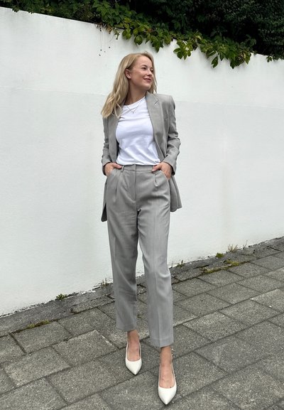 Traje gris claro con una chaqueta a medida y pantalones rectos, combinado con una camiseta blanca y zapatos de tacón en crema. Textura suave.