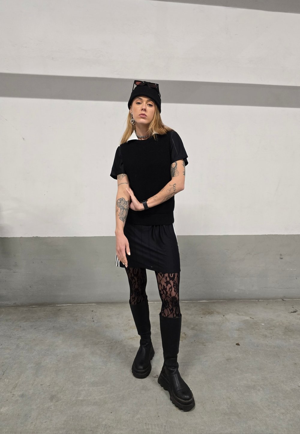 Sort strikket vest over en sort t-shirt, parret med leggins med blonder og knæhøje sorte støvler. Tilbehøret inkluderer en sort hue og solbriller.