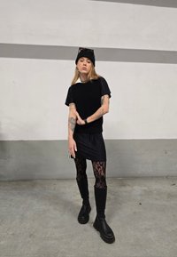 Sort strikket vest over en sort t-shirt, parret med leggins med blonder og knæhøje sorte støvler. Tilbehøret inkluderer en sort hue og solbriller.