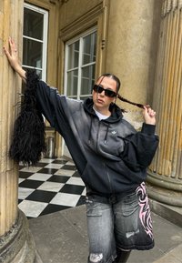 Hanorac cu gradient negru și gri cu logo alb, asortat cu pantaloni scurți din denim uzat cu modele roz. Accente din blană artificială neagră.