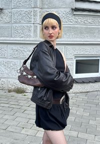 Μαύρο μπομπερ μπουφάν πάνω από ένα αμάνικο μαύρο φόρεμα, με καφέ τσάντα χειρός που διαθέτει ασημί αξεσουάρ και υφασμάτινο μοτίβο. Ορατές καλσόν με δίχτυ.