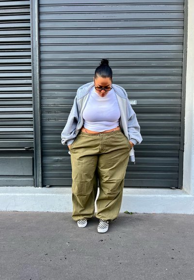 Sudadera oversized gris claro, top corto blanco y pantalones de pierna ancha verde olivo, combinados con zapatillas de cuadros en blanco y negro.