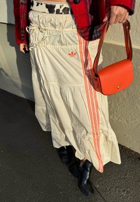 Fløjlsfarvet lagdelt nederdel med orange side-striber og et Adidas-logo, kombineret med en lille orange håndtaske og sorte ankelstøvler.