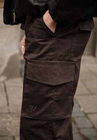 Braune Cargo-Hosen mit mehreren Taschen, einem strukturierten Stoff und einem seitlichen, bestickten Logo. Eng anliegender Schnitt mit dezentem Glanz.