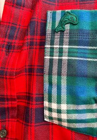Tecido de flanela xadrez vermelho e azul marinho com um bolso de padrão de xadrez verde e azul. Detalhe bordado verde notável no bolso.