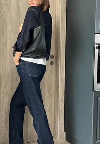 Μαύρη δερμάτινη τσάντα tote με χαλαρή σχεδίαση και μαλακή υφή, συνδυασμένη με σκούρο μπλε τζιν και ένα στιβαρό λευκό πουκάμισο από κάτω.