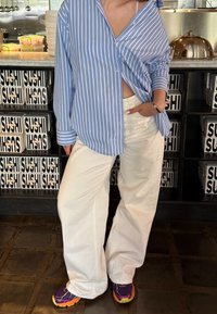 Light blue and white striped shirt with rolled sleeves, paired with loose white trousers and purple trainers with yellow accents.
