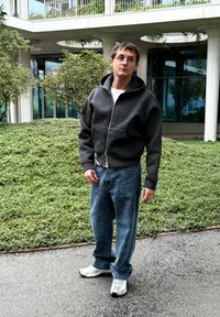 Pilka užtraukiama su gobtuvu sportinė apranga su didele gaubtu, dėvima ant balto marškinėlio, derinama su šviesiai mėlynomis džinsinėmis kelnėmis. Atrodo patogios sportinės avalynės.