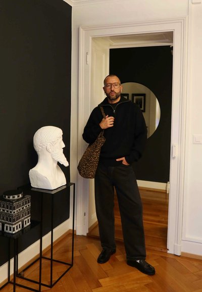 Bolso de hombro con estampado de leopardo, suéter negro y pantalones oscuros. Busto de mármol blanco sobre un soporte negro al lado de un recipiente decorativo en blanco y negro.