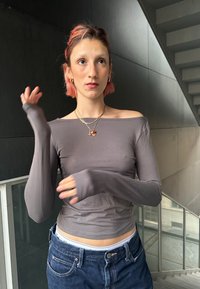 Top de manga larga gris con diseño de hombros descubiertos, ajuste ajustado y textura suave. Llevado con jeans oscuros, que presentan un estilo casual y un collar en capas.