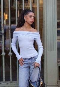 Lyseblå off-shoulder ribbet top med lange ærmer, kombineret med højtaljede lyse denimjeans og en sort skinnende håndtaske.