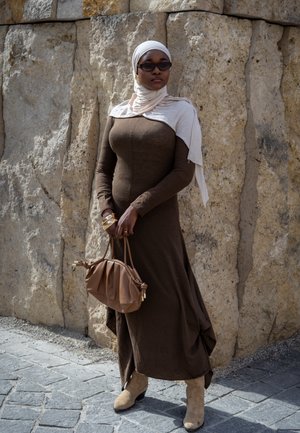 Vestido marrón de manga larga con tejido texturizado, pañuelo ligero beige, bolso marrón con detalles fruncidos, y botas de tobillo color beige.