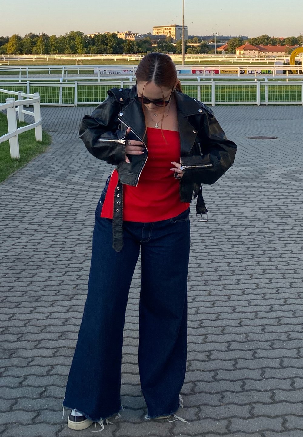 Svart skinnjakke, rød tanktopp og vide mørk denim-jeans. Klar himmel, steinlagt vei og grønt gress i bakgrunnen.