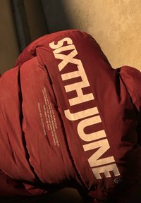 Μαρό νάιλον μπουφάν με μεγάλο λευκό κείμενο "SIXTHJUNE" και μικρότερες εκτυπωμένες λεπτομέρειες. Υφασμάτινη επιφάνεια με καπιτονέ τμήματα. Στρογγυλή λεπτομέρεια λογότυπου.