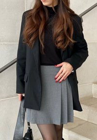 Μαύρο σακάκι πάνω από μαύρο λαιμόκοψη, συνδυασμένο με γκρι πλισέ φούστα. Διαθέτει μαλακό ύφασμα, κοφτή κατασκευή και δομημένη σιλουέτα.