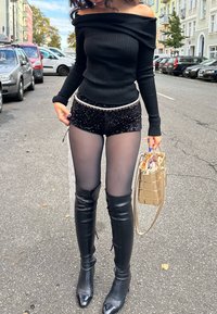 Czarny prążkowany top bez ramiączek, świecące czarne szorty, przezroczyste czarne rajstopy, wysokie czarne botki oraz złota torebka na łańcuszku.