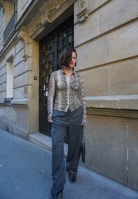 Ormtryckt blus med lång ärm och knappstängning, kombinerad med grå byxor med hög midja. Looken fulländas med svarta stilettklackar och en svart väska.