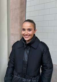 Czarna puchowa kurtka o połyskującej powierzchni, z wysokim kołnierzem, odpinanym paskiem w talii i usztywnionymi ramionami; gładka faktura.