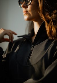 Black zip-up jacket with a ribbed texture, high collar, and a subtle sheen. It features a zip closure and a minimalist design with no patterns.