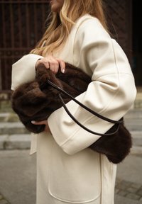 Hnedá kabelka z umelej kožušiny s mäkkou textúrou, vybavená dlhým koženým remienkom. Nosí sa s krémovým, štruktúrovaným kabátom.