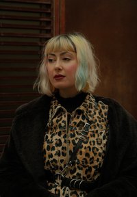 Leopardmønstret denimjakke med en sort turtleneck, parret med en fuzzy sort frakke. Har hoop øreringe og hår i forskellige farver.