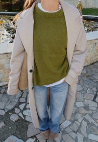 Béžový trenčkot cez zelený pletený sveter, biele tričko a svetlomodré nohavice s širokými nohavicami; hnedé slip-on topánky s textúrovanou podrážkou.